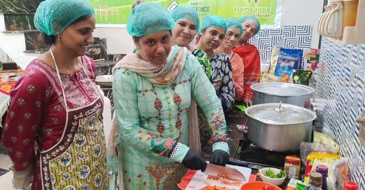 Women in aprons and hairnets preparing food together in a Ghar Ka Zaiqa central kitchen